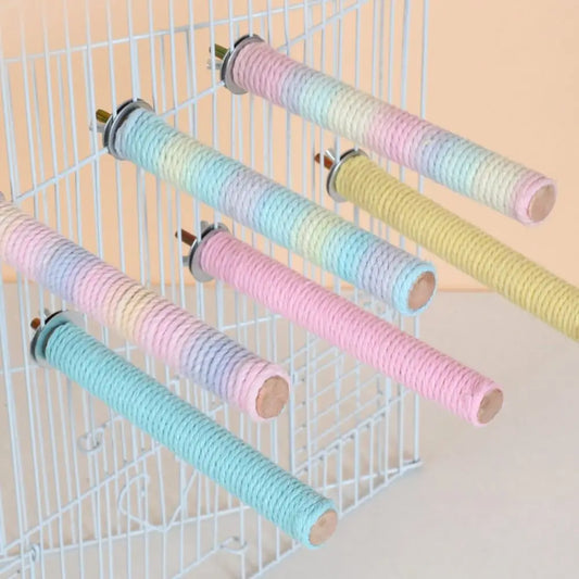 Six pastel rope bird perches wrapped in pastel rainbow-colored rope, mounted on a white wire cage against a light peach background.
