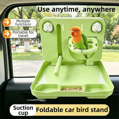 A light green foldable car bird stand with a suction cup attachment, shown mounted inside a car window. A small green and orange bird is perched on the stand, and birdseed is visible in the tray.