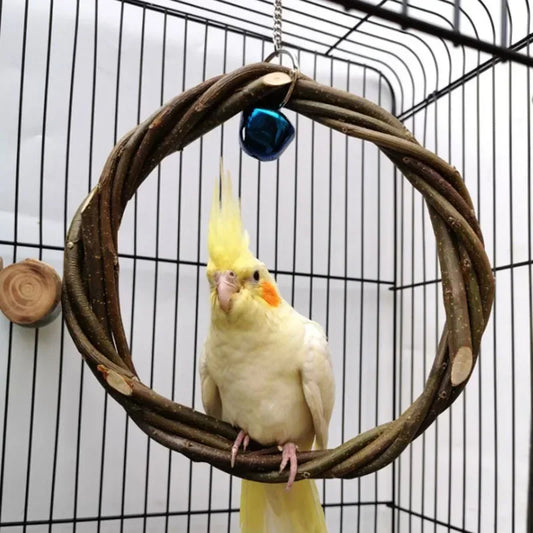 A yellow cockatiel perched inside a circular twig bird toy hanging in a cage. The toy is made of intertwined branches with small flat wood tabs and a small blue bell at the top.