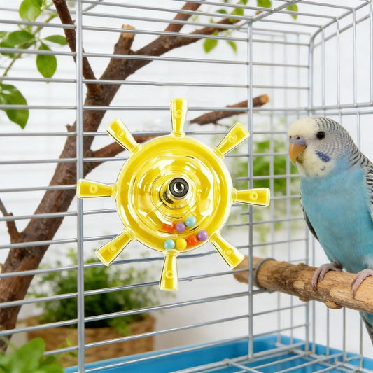 A blue and gray budgerigar perched on a wooden branch inside a metal bird cage, next to a yellow ship-wheel shaped toy with small colorful beads.