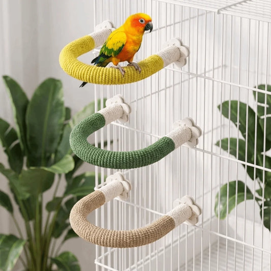 Three curved bird perches wrapped in yellow, green, and beige rope hang inside a white wire cage, with a small yellow-and-green parrot perched on the top yellow perch.