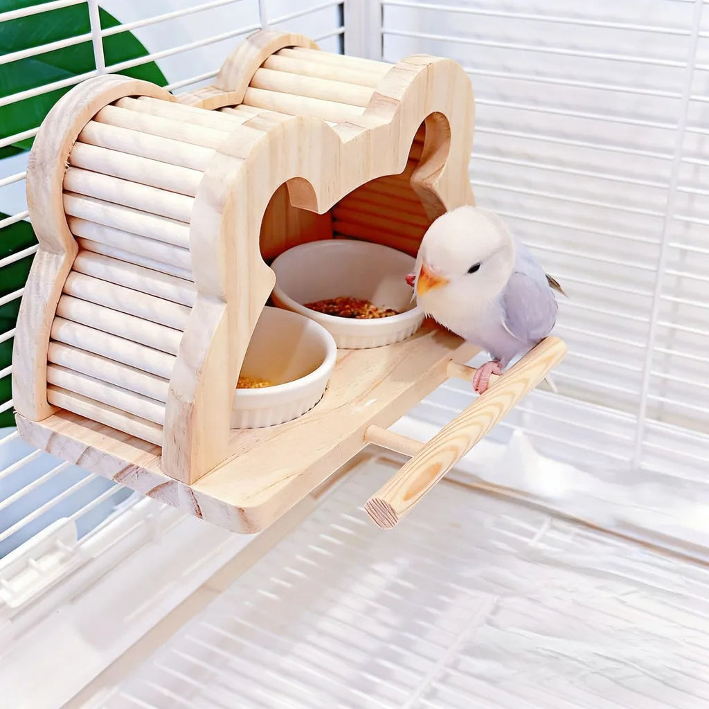 A small white and gray bird perched on a wooden bird feeder and perch inside a cage, with two white bowls containing food.