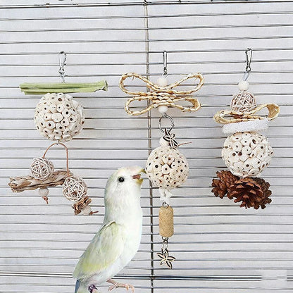 Bird perched on a branch with a bird toy featuring natural elements like pine cones and rattan balls.