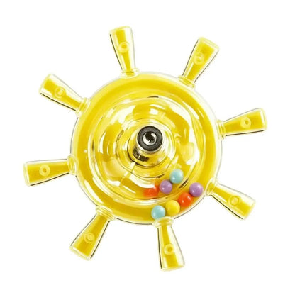 A yellow ship's wheel toy with a clear plastic center, a metal axle, and small multicolored beads inside, shown on a plain white background.