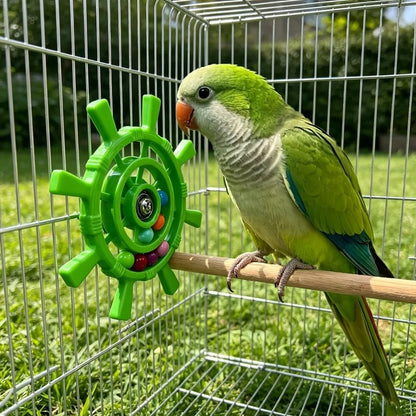 A green parrot perched on a wooden bar inside a wire cage, next to a bright green ship-wheel style toy with colorful beads. Grass and trees are visible in the background.