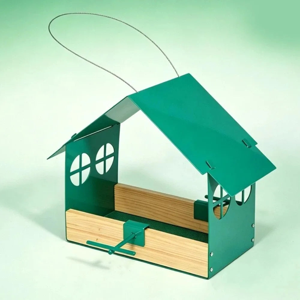 A metal birdhouse feeder with a green tin roof and sides, natural wood interior tray, and a wire hanging loop, shown on a pale green studio background.