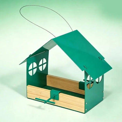 A metal birdhouse feeder with a green tin roof and sides, natural wood interior tray, and a wire hanging loop, shown on a pale green studio background.