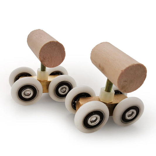 Two small wooden bird skates  with cylindrical wood tops, brass-colored metal bodies, and white wheels with black inner rings, photographed on a clean white background.